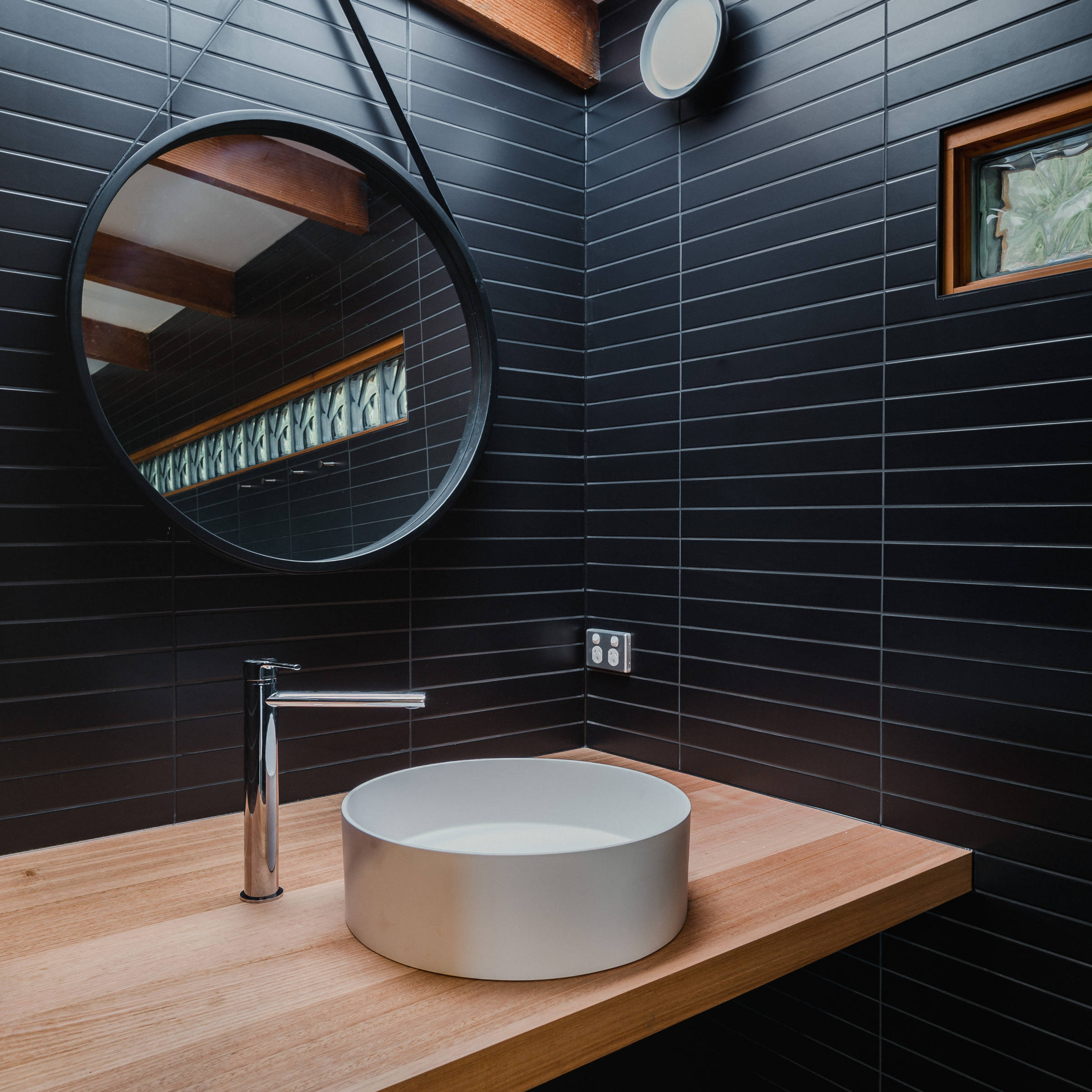 Custom Japanese inspired bathroom renovation featuring black mosaic tiles, hanging mirror, custom timber benchtop in Tasmanian oak. The architectural bathroom renovation was designed to give a contemporary feel and also features a round white basin with increased natural light from a new skylight. Photo: Jordan Davis.